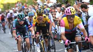 The peloton, wearing bright pink, yellow and green cycling helmets, complete for the lead in a road race leading up to the 107th Giro dell&#039;Emilia 2024