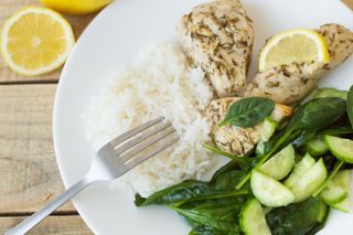 A plate containing chicken breasts with lemon, rice, spinach and cucumber salad.