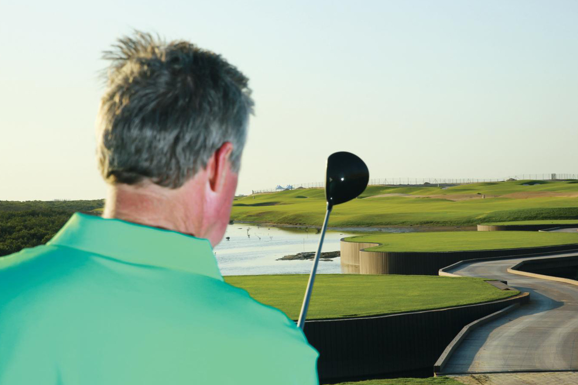 An over the shoulder look down the golf course from the tee box, with the driver outstretched picking a small target to present the mantra of aim small, miss small