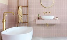 Pink tiled bathroom with white tub, gray flooring and gold accents including a wall mirror