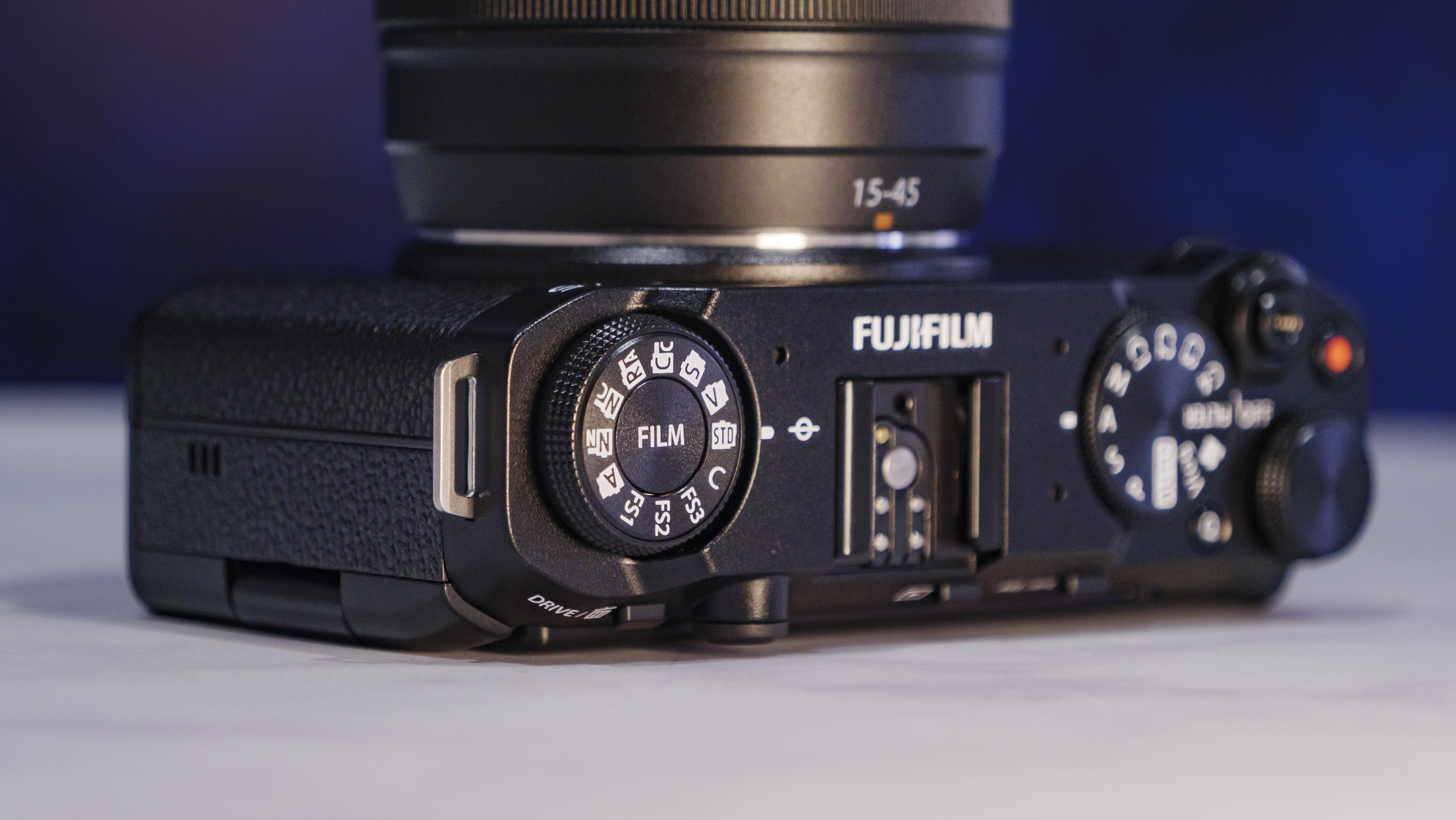 Closeup of the Fujifilm X-M5 camera's top plate,  on a marble surface with rich blue background