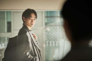 a man (Masaki Suda as Shinichi Izumi) wears a backpack in a sunny office, in 'parasyte the grey'