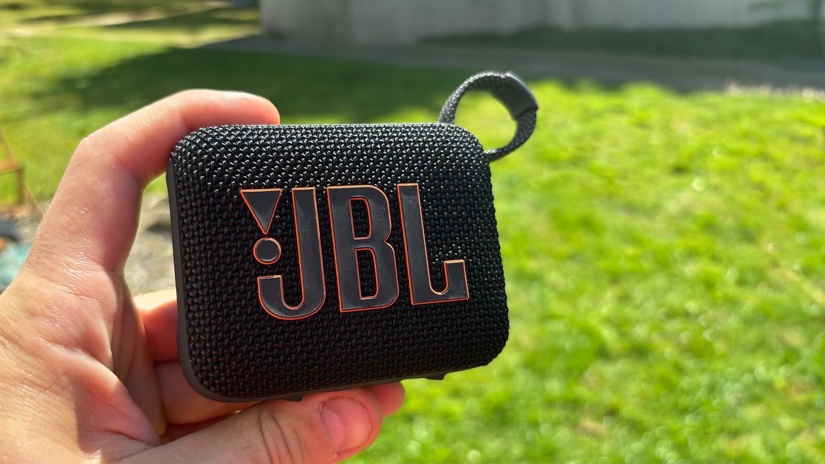 JBL Go 4 Bluetooth speaker held in hand over green grass