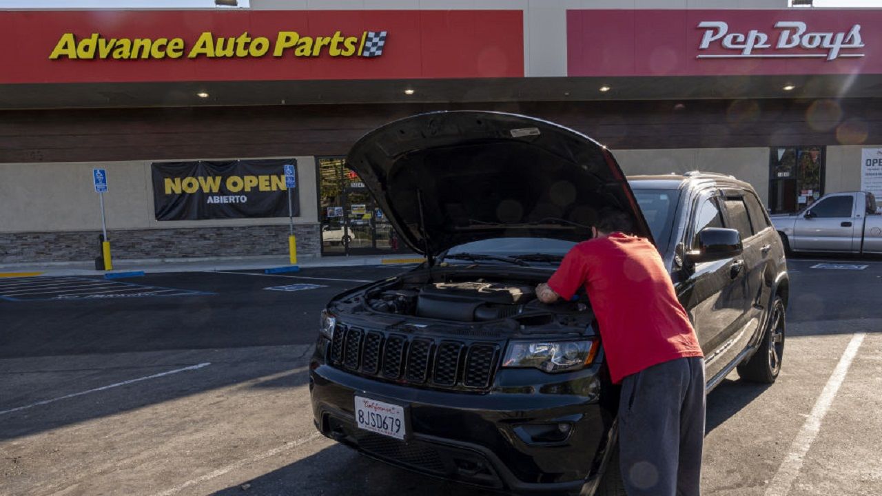 Man working under the hood of car parked in Advance Auto Parts store parking lot.