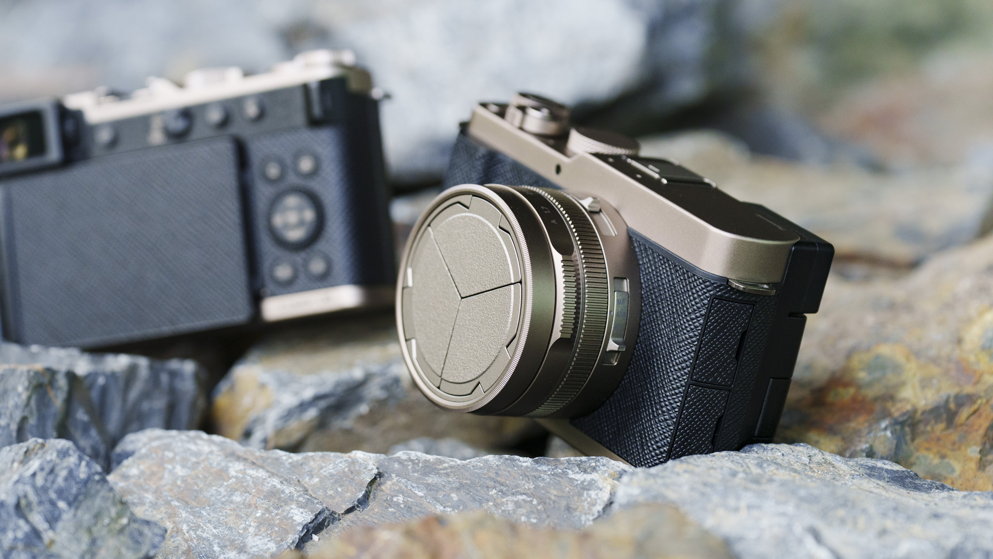 The Gold Titanium Special Edition of the Panasonic Lumix L10 compact camera, sat on gray and rust-colored rocks