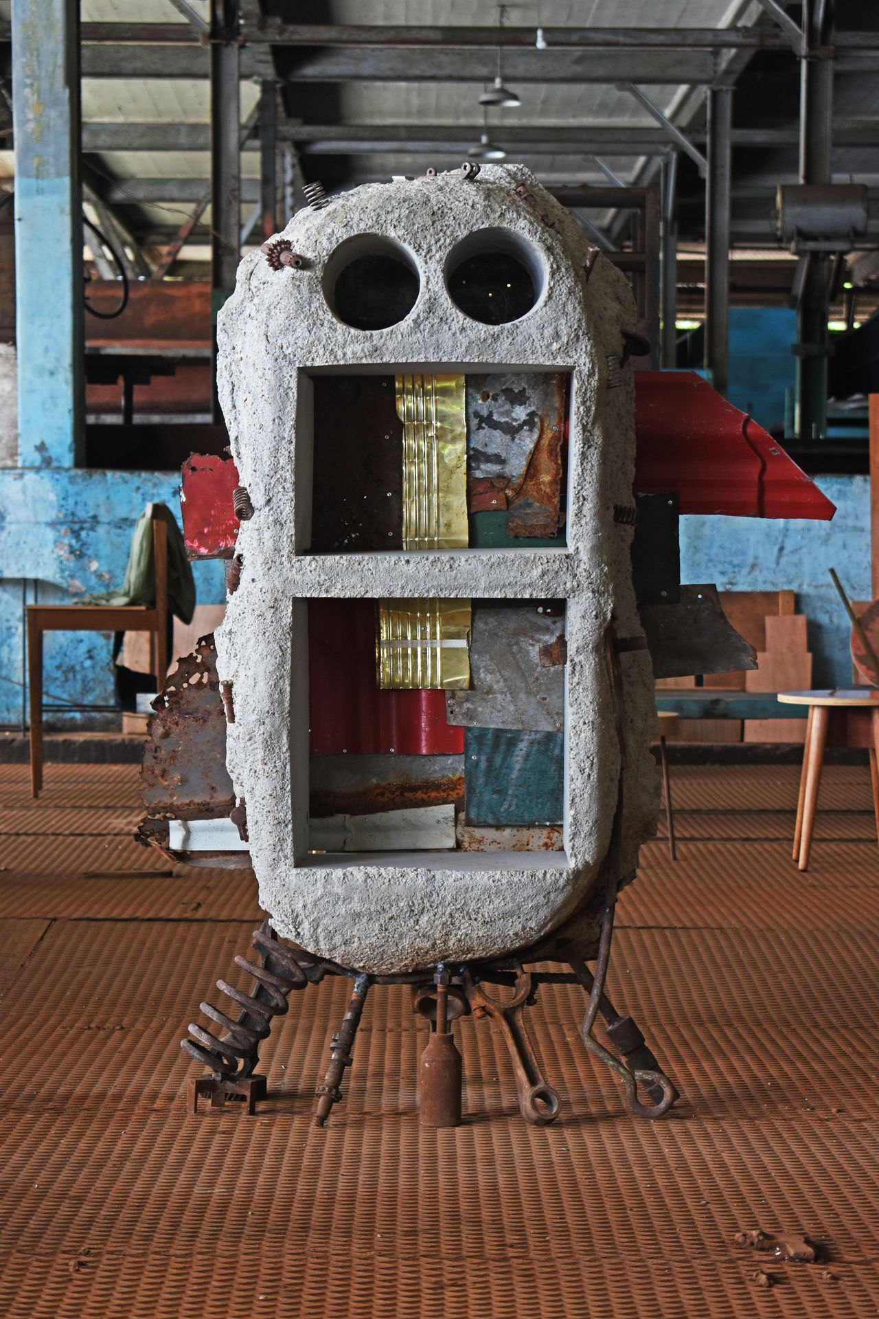 A whimsically designed, creature-like shelving unit is casted out of discarded metal fragments and rock-looking material to resemble a face.