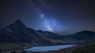 large peaks surround a lake in the foreground with the milky way bulge stretching up into the starry sky above.