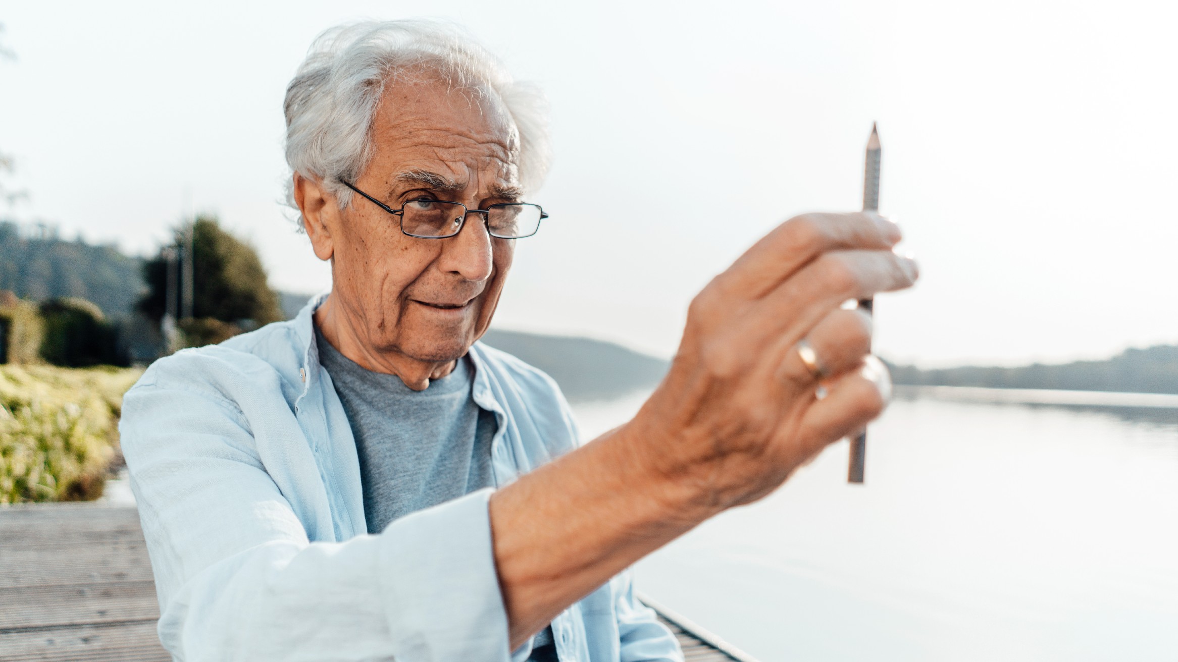 An elderly man demonstrating that parallax can be demonstrated by looking at a pencil with one eye closed.