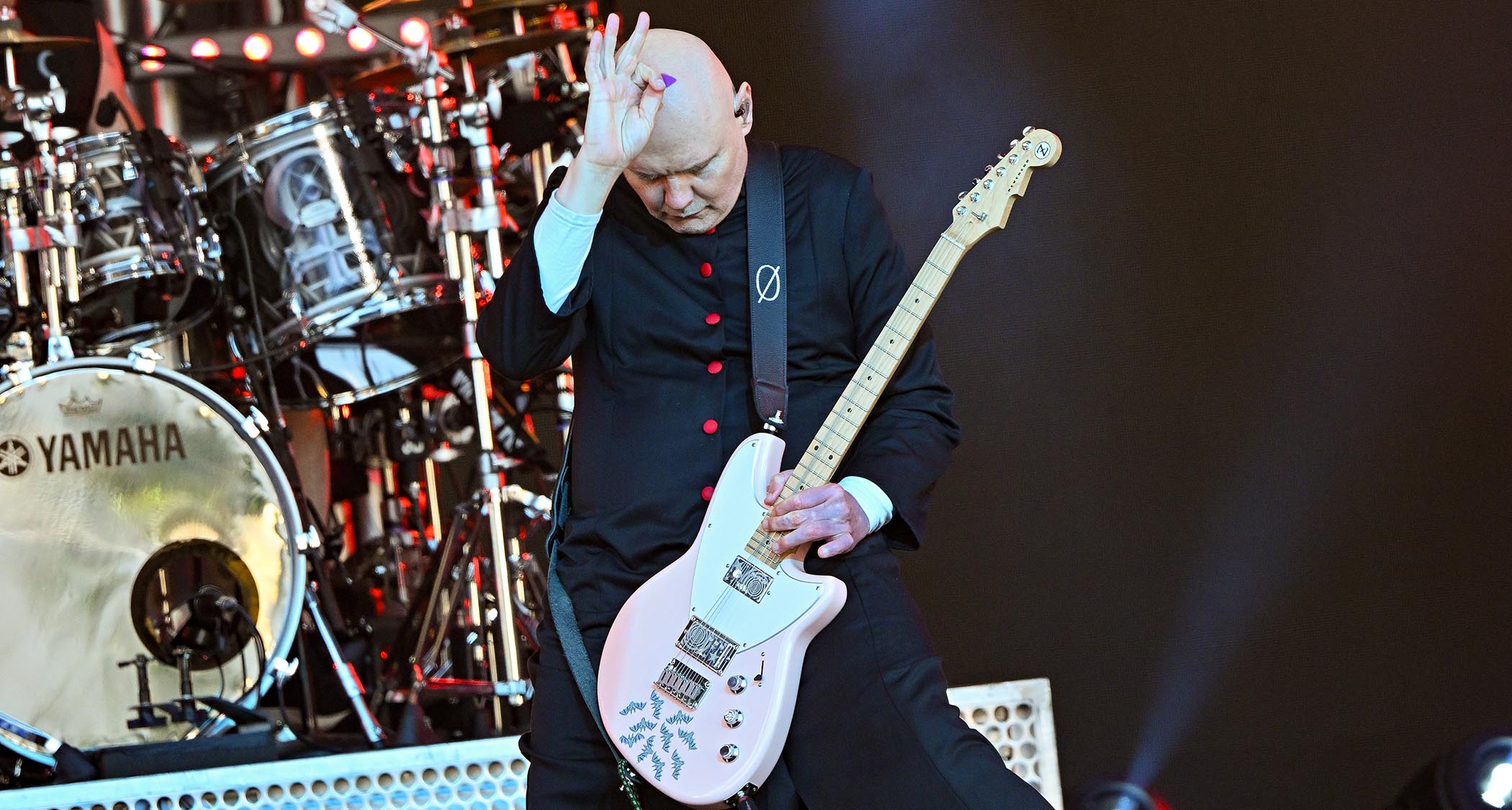 Billy Corgan holds his picking hand to his head as he holds a note on his Reverend signature model