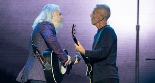 Tears For Fears' Roland Orzabal [left] and Curt Smith perform live on the band's Tipping Point tour, with pastel-coloured stage lights and video in the background.