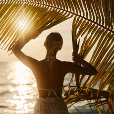 Summer perfumes: a woman stands under a palm tree at beach