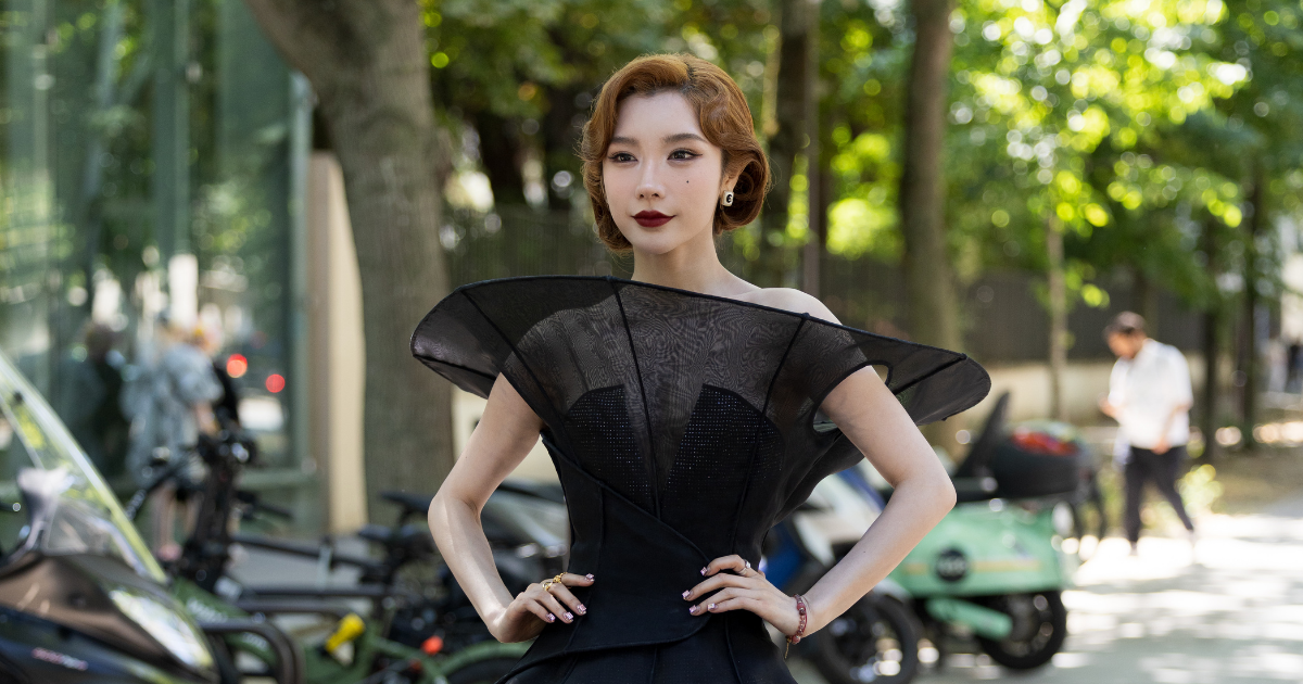 Summerween Gothic Glam Makeup Beauty: Dai Yanni wears a sculptural black mini dress featuring exaggerated fan-like shoulder structures, a fitted bodice,
