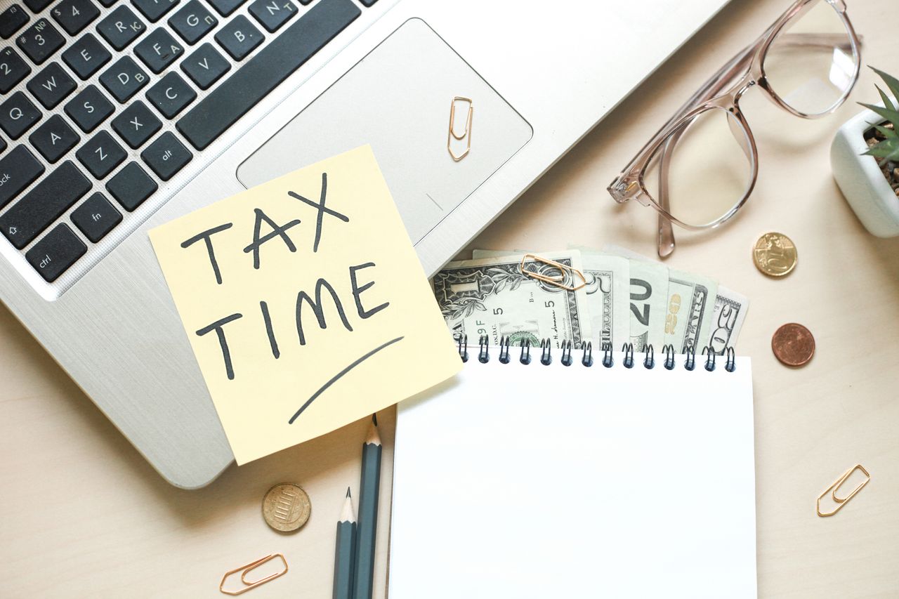 computer and various desk accessories as well as money, with post it note that reads &#039;Tax Time&#039;