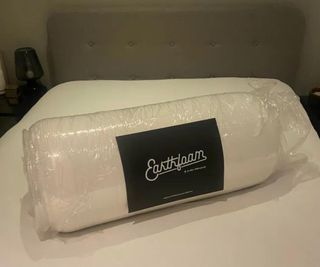 The Earthfoam Mattress Topper rolled up in plastic wrap on a bed.