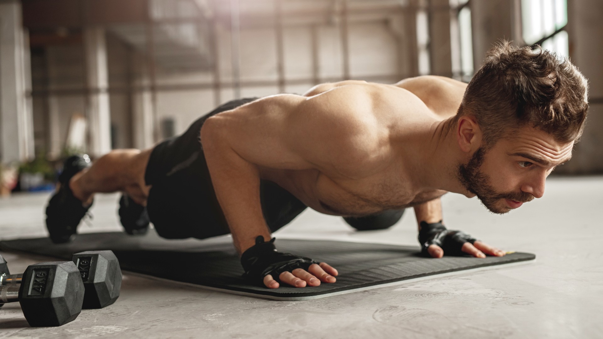 Man performing a push-up during workout with dumbbells next to him