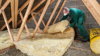 man wearing green overalls and face mask laying insulation on loft floor
