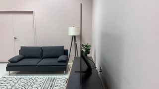 Samsung S95C TV on stand seen from the side with gray wall in background