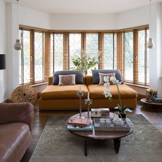 A white living room with wooden bay window frames wooden flooring and brown leather sofas