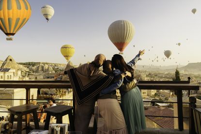 Three ladies standing on a balcony watching hot air balloons
