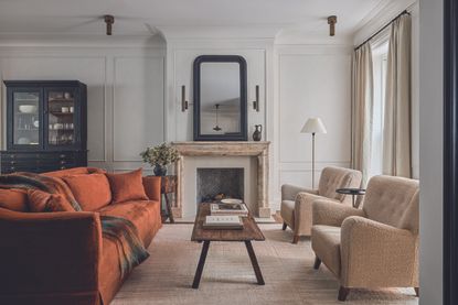 A cream living room with a wooden coffee table, orange accent sofa and neutral palette. 