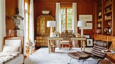 Home office with wood bookshelf, midcentury leather chair, gilded desk and cabinet and large lamps
