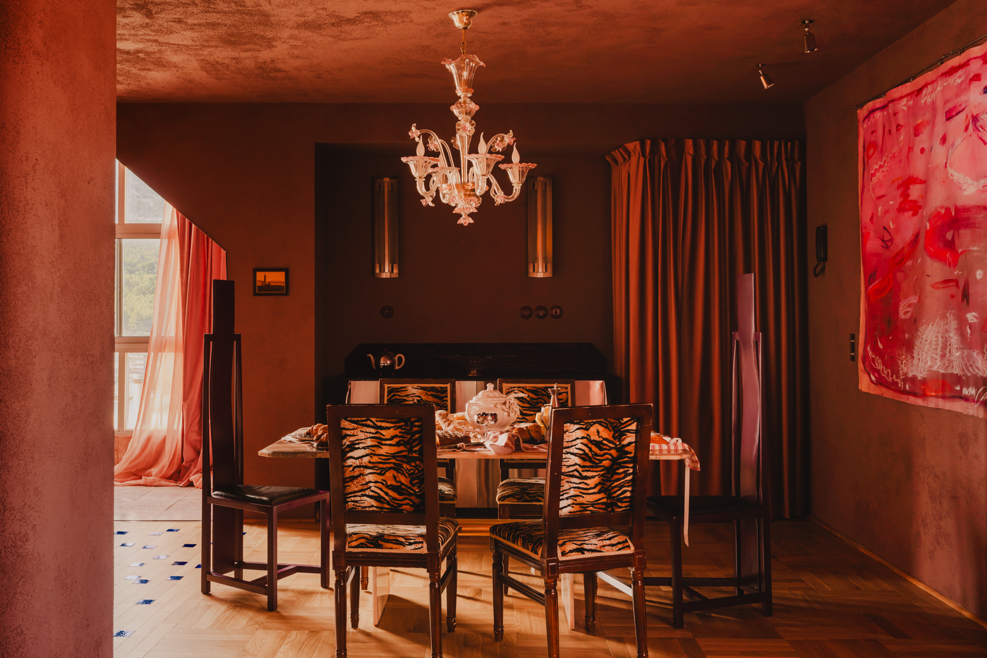 A dining room with tiger-print upholstered chairs beneath a Murano glass chandelier.