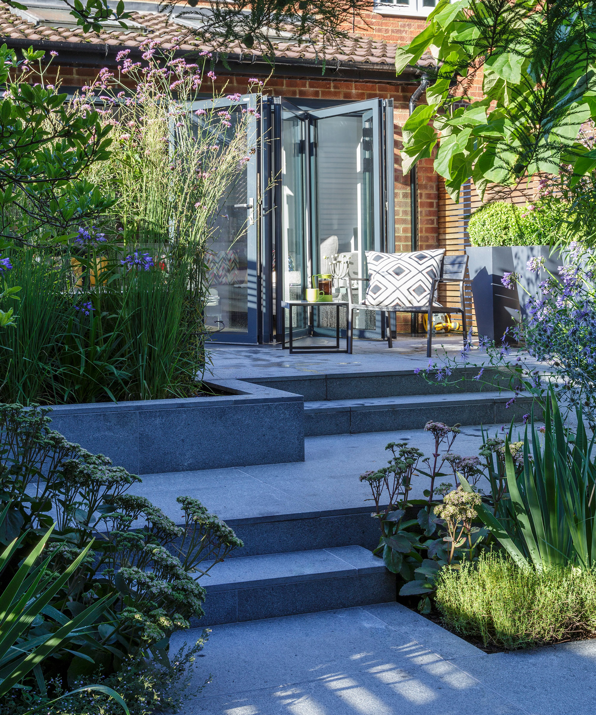 A gray garden patio area with steps leading up to a bistro table and chair set