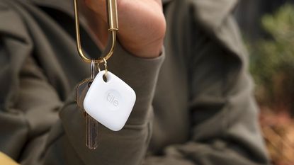 Woman dangling white Tile key finder attached to gold key chain