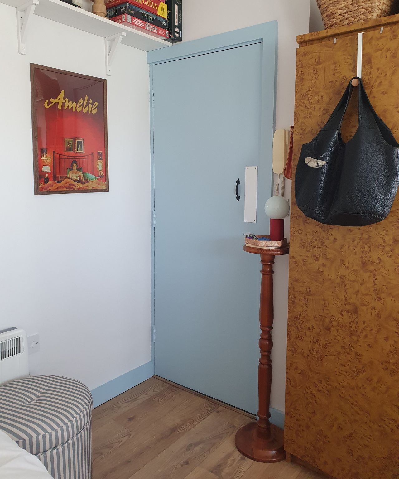 After: Sara's entrance area with a striped storage ottoman, a side table with a lamp next to the front door and a framed film poster hanging on the wall