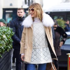Bella Hadid wearing a tan coat, cream sweater, cropped flare jeans, socks, and loafers in Paris during PFW F/W 26