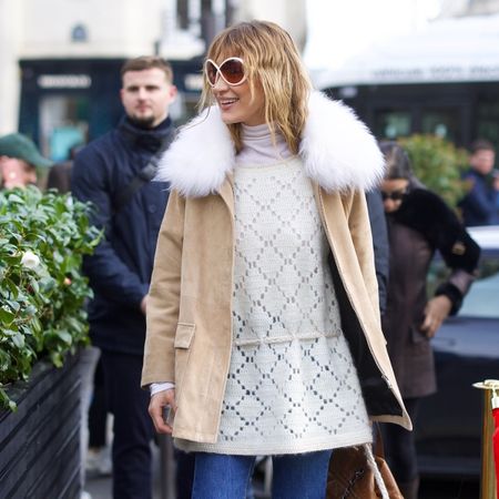 Bella Hadid wearing a tan coat, cream sweater, cropped flare jeans, socks, and loafers in Paris during PFW F/W 26