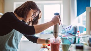Woman making berry smoothie with stick blender