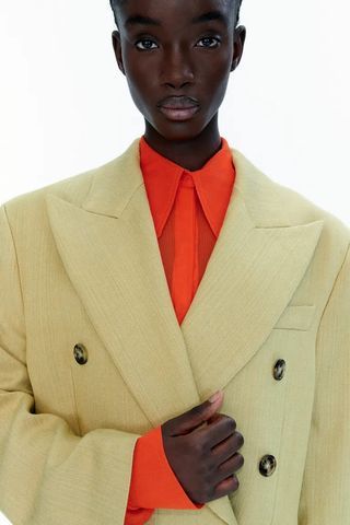 H&M model wearing an orange mesh button-down shirt with a tan coat.