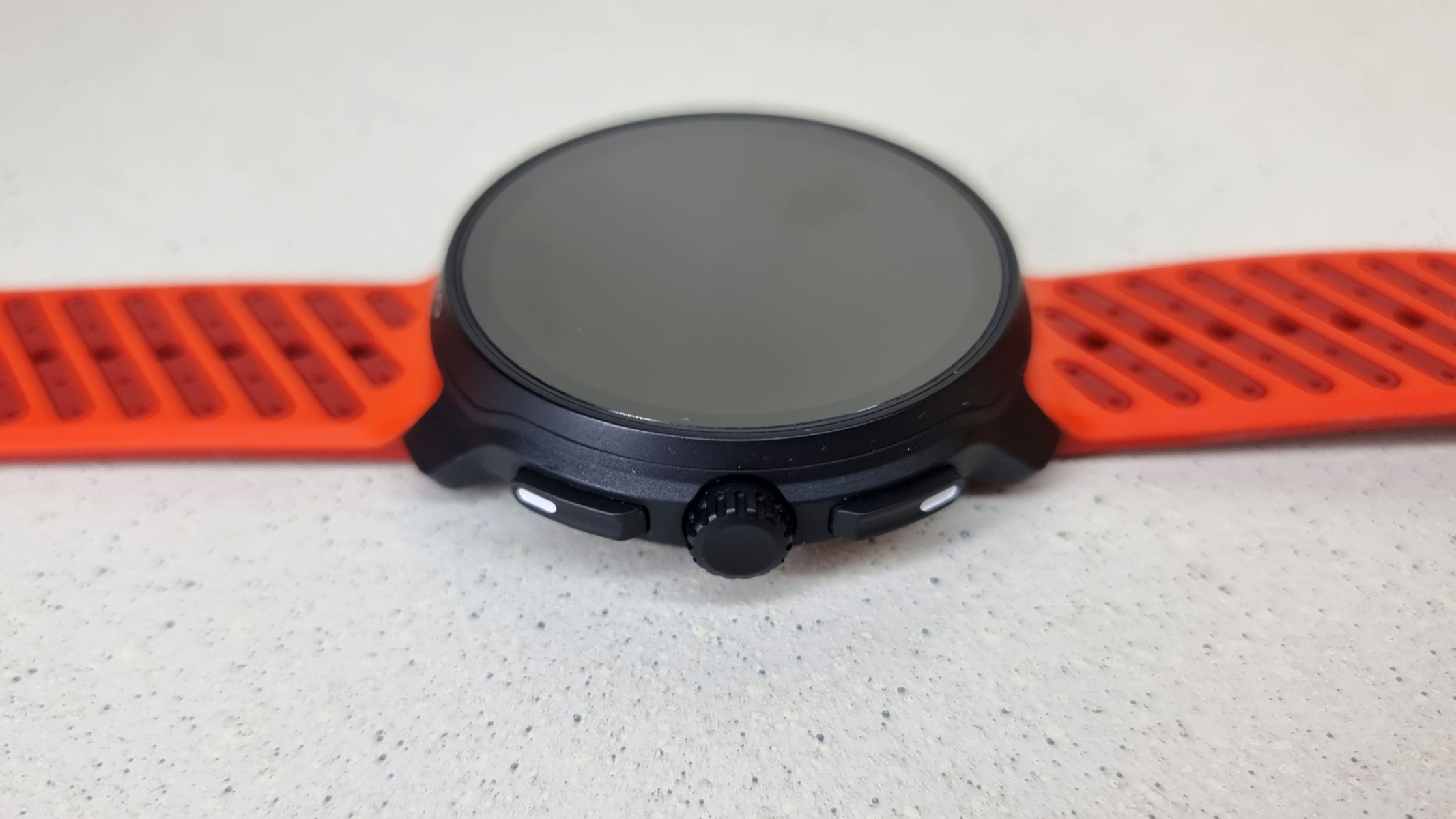 The Suunto Race 2 with orange strap lying front side up on a white surface.