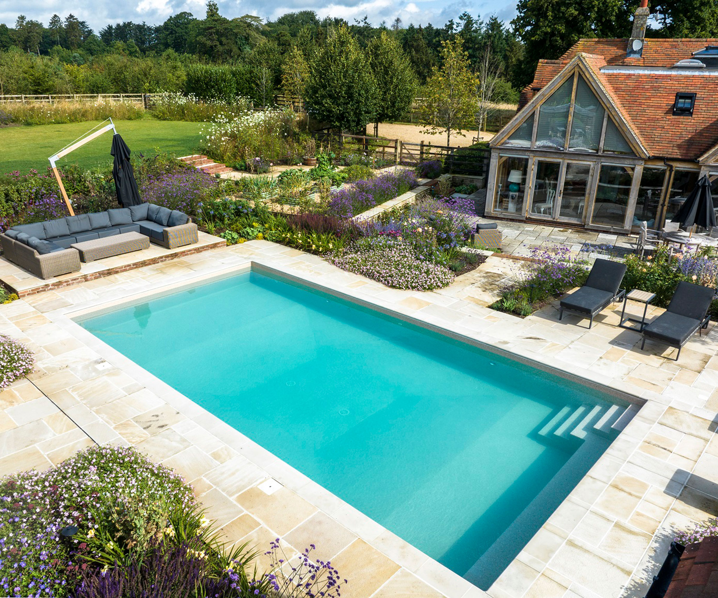 large swimming pool with patio surround, garden sofas, sun loungers and planting