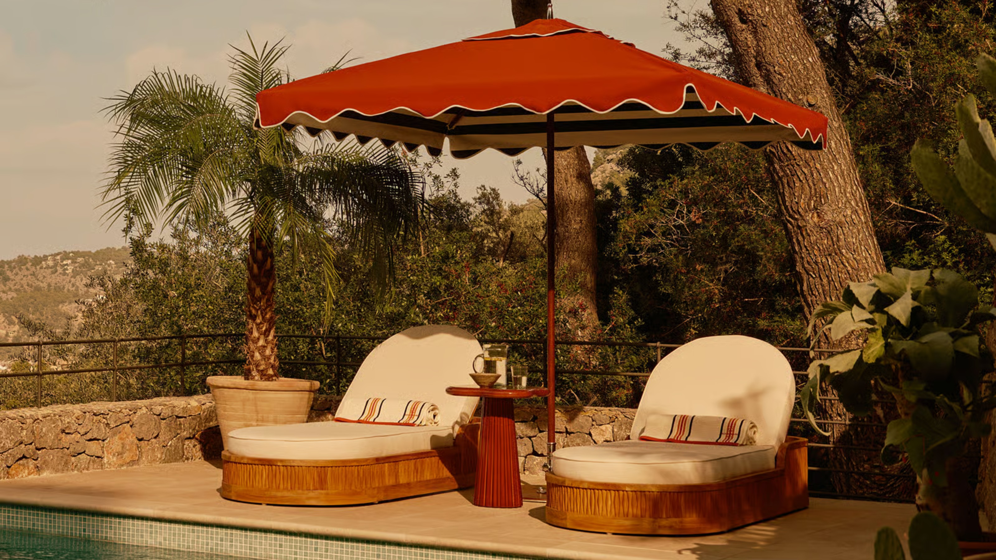 Soho Home's curved sun loungers and a red parasol by the pool