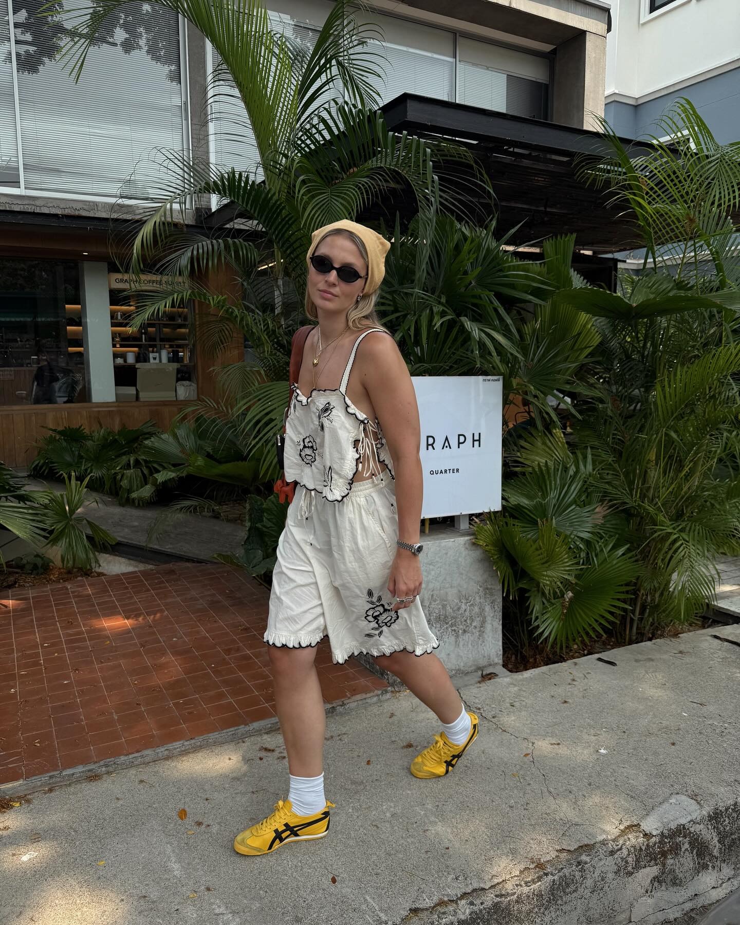 Fashion person Hollie Mercedes wears a linen set with yellow Onitsuka tiger, a silk scarf and oval sunglasses in a recent image taken from her Instagram.