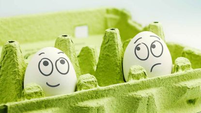 Two eggs in an egg carton: One with a happy face drawn on and one with a sad face.
