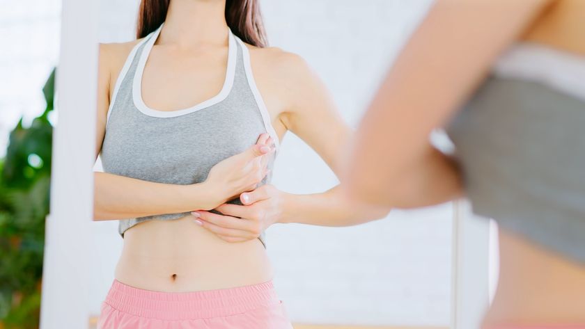 A woman stands in front of a mirror and palpates her breasts during a cancer self-check