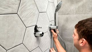 Man installing a shower head in bathroom with grey hexagonal tiles
