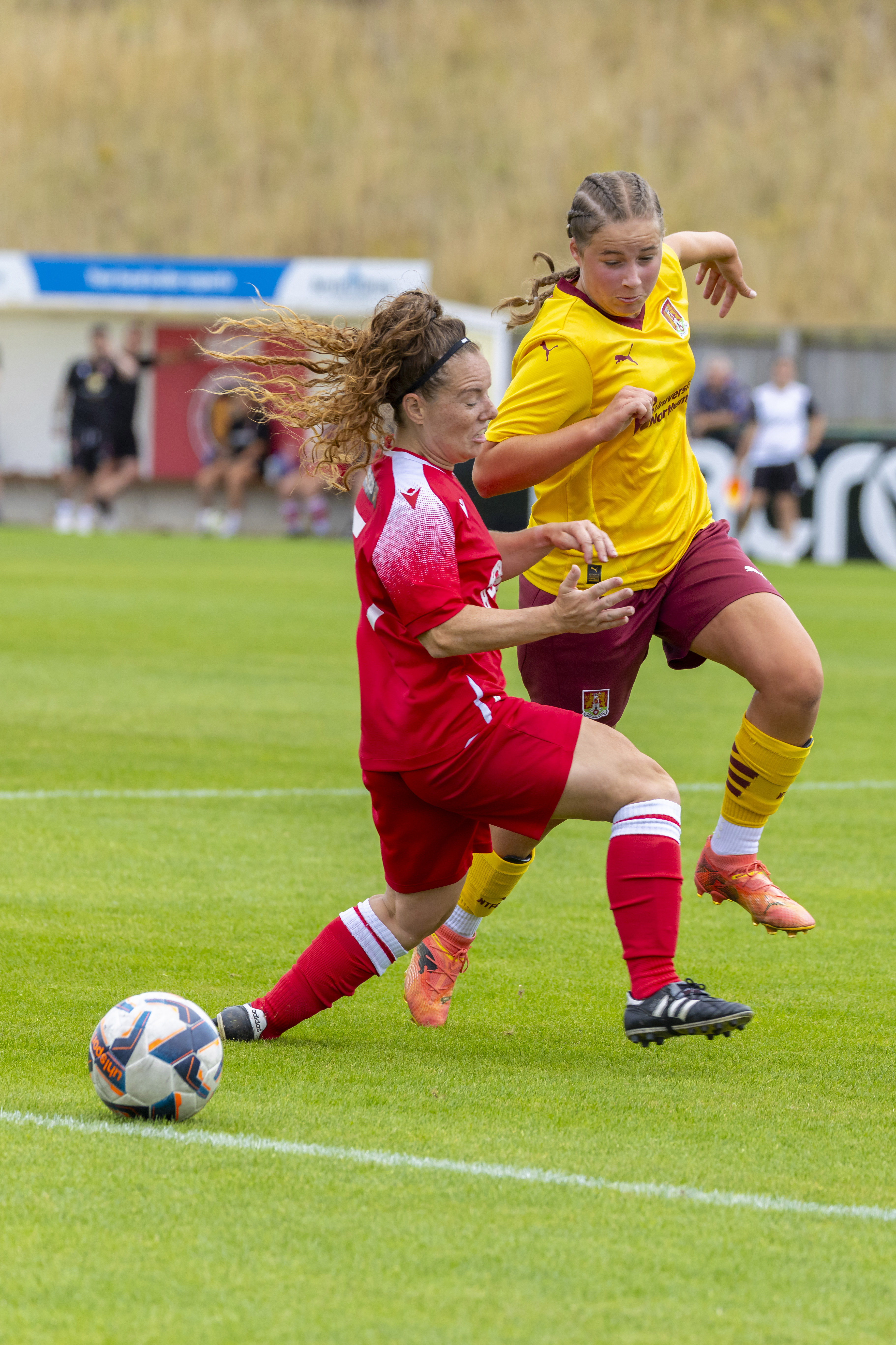 A picture of two soccer players involved in a tackle, one is wearing red while the other is wearing yellow colors