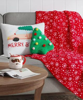 A sofa with a Christmas throw, Christmas pillows, and a Santa mug on a coffee table