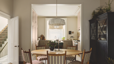 a dining room with a round dining table, five chairs, and a tall black hutch to the right, and a kitchen in the background 