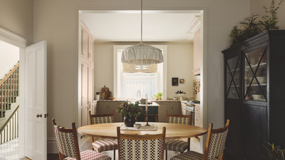a dining room with a round dining table, five chairs, and a tall black hutch to the right, and a kitchen in the background 