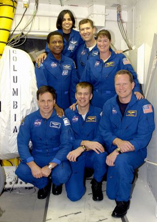 The STS-107 crew poses in front of the hatch into space shuttle Columbia. Kneeling in front (left to right): payload specialist Ilan Ramon, pilot Willie McCool and mission specialist David Brown. Standing in the back: mission specialists Michael Anderson and Kalpana Chawla, commander Rick Husband and mission specialist Laurel Clark.