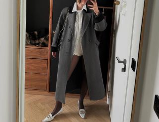 @BETTINALOONEY wearing a gray long coat with a button-down shirt, hot pants, tights, and white kitten heels.