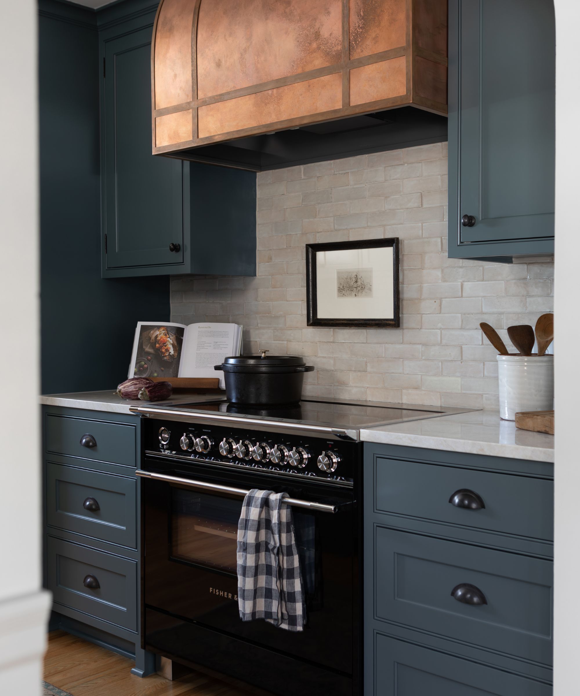small galley kitchen painted navy blue with a black stove, copper cooker hood and vintage decor