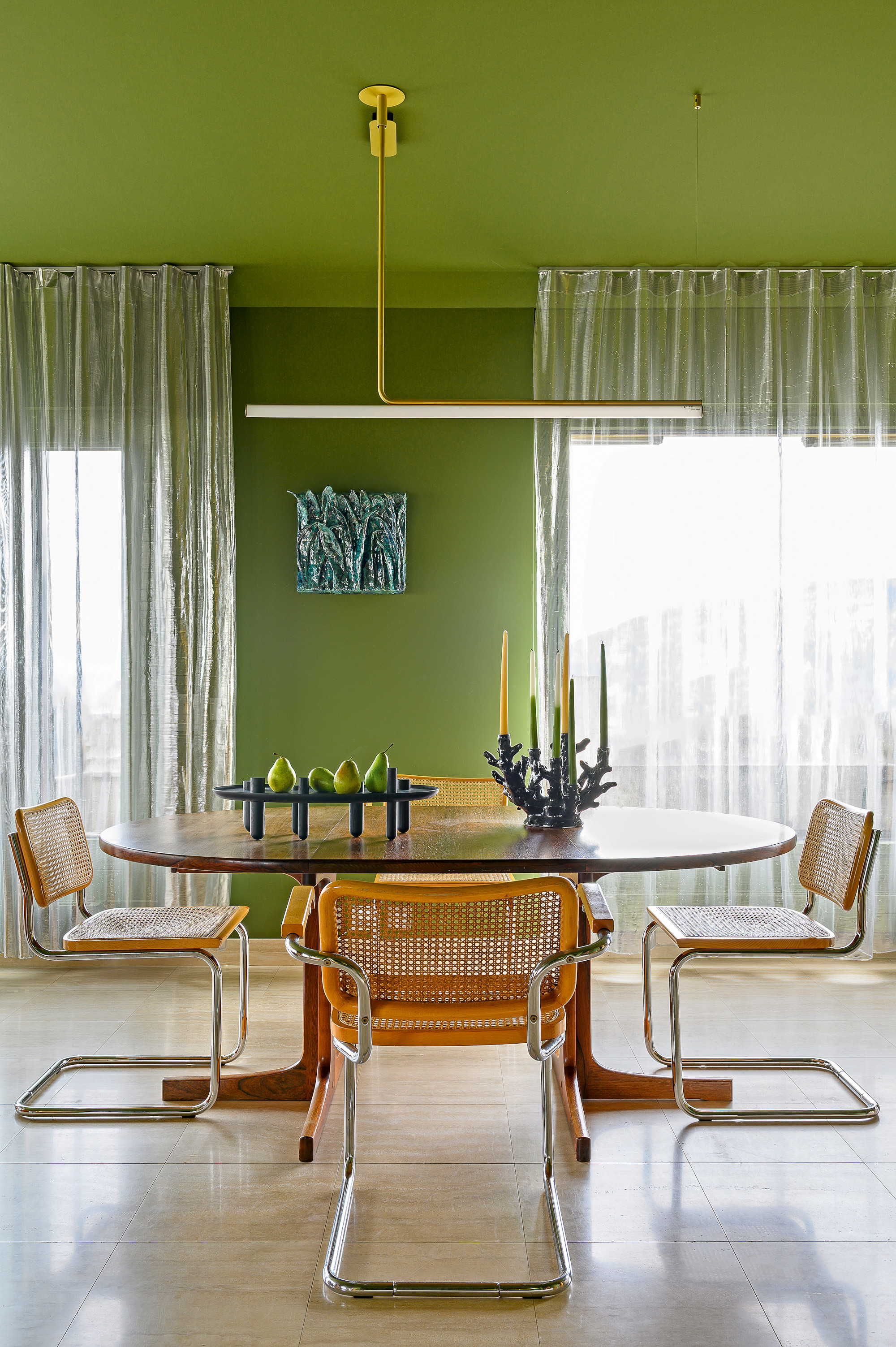 Matcha green living room with oval wood table, chrome and cane chairs and linear pendant light
