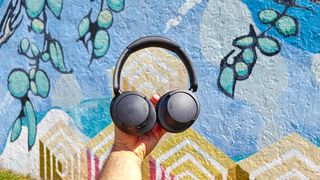 best cheap headphones listing image showing 1More SonoFlow SE held up against a colorful backdrop