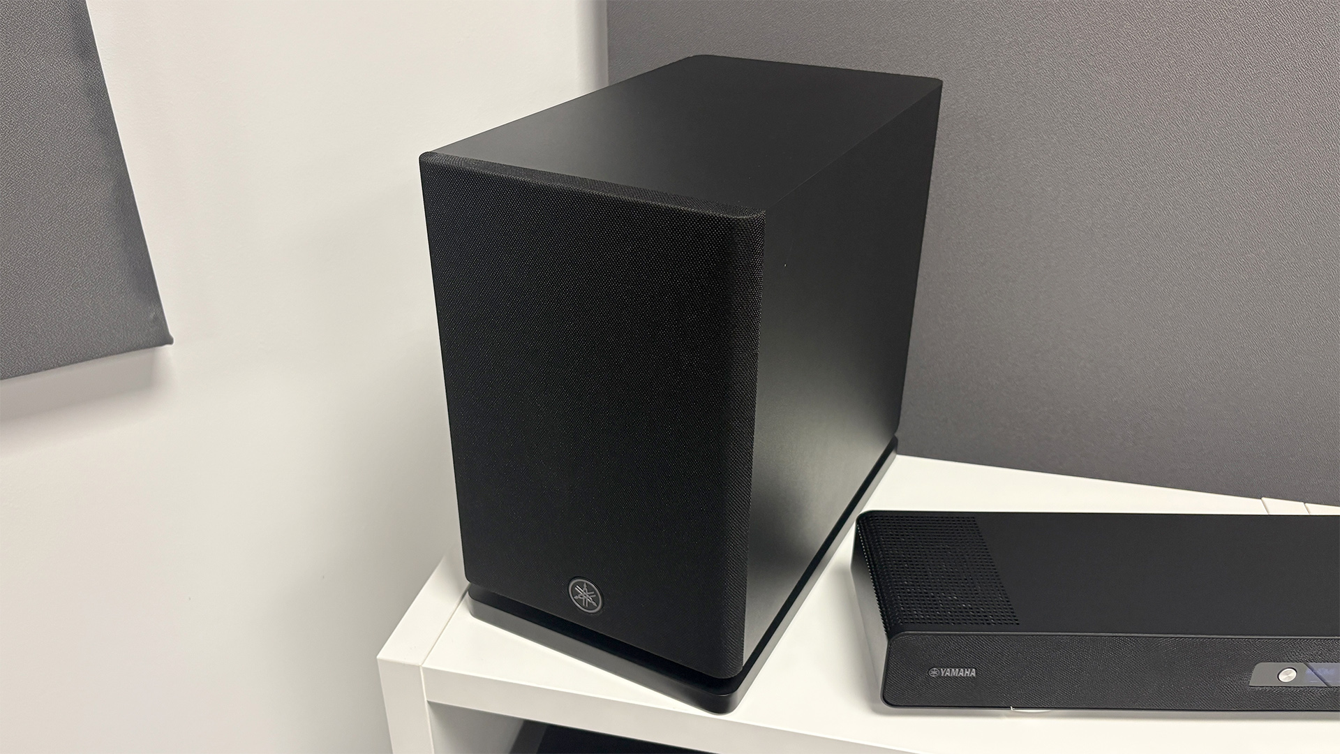 Yamaha True X Surround 90A soundbar package subwoofer on white shelf unit next to soundbar
